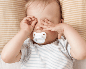 müdes Baby mit Schnuller reibt sich die Augen