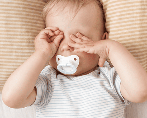 müdes Baby mit Schnuller reibt sich die Augen